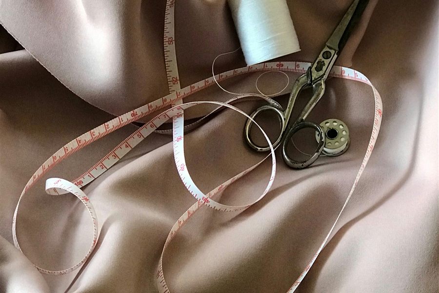 Mètre ruban, ciseaux de couturière et bobine de fil posés sur un tissu